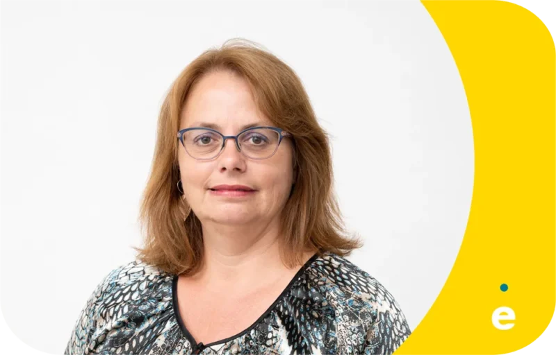 Portrait d'une femme aux cheveux bruns portant des lunettes et un haut à motifs noirs et blancs, sur fond blanc avec un coin jaune.