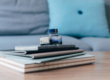 Des carnets empilés sur une table en bois avec un flacon d'encre bleu, en arrière-plan un canapé gris avec un coussin bleu.
