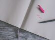 Carnet ouvert avec lignes, stylo noir et capuchon rose sur une table en bois grise, texte "START TODAY" écrit en rose.