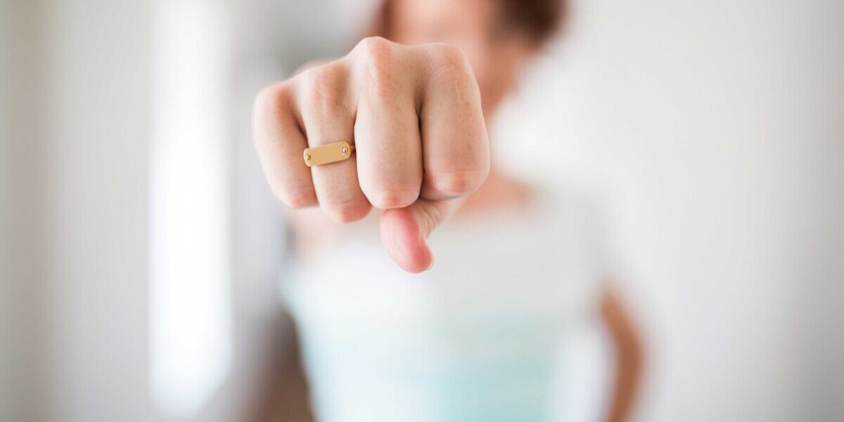 le féminisme Une personne tend le poing vers l'objectif, portant une bague dorée sur fond flou.