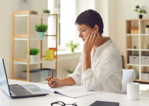 une femme réfléchit en regardant son ordinateur elle ne connait pas son archétype financier