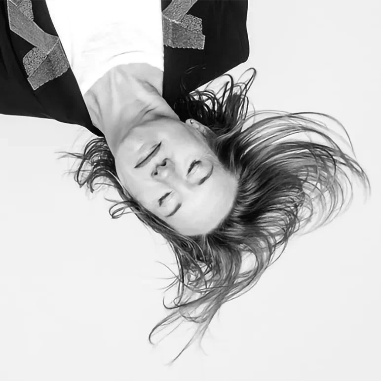 Personne aux cheveux longs étendue sur le dos, portant un haut blanc et une veste noire à motifs géométriques.