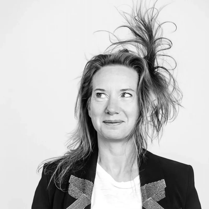 Personne aux cheveux ébouriffés portant une veste noire avec motifs brillants sur fond blanc.