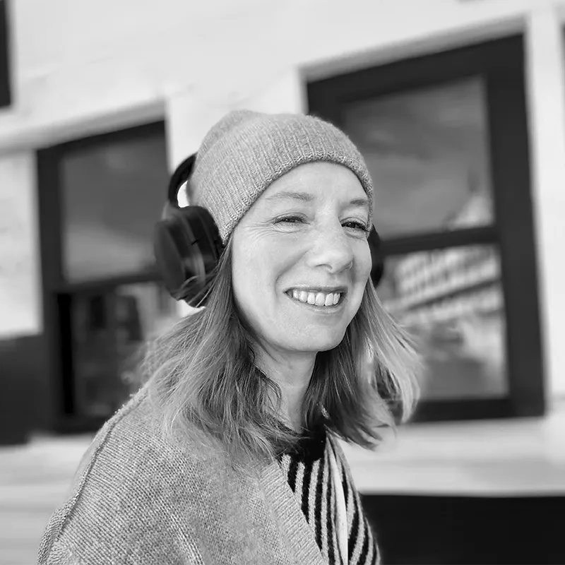 Une personne souriante portant un bonnet et un casque audio noir devant un bâtiment avec des fenêtres.